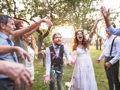 Bride, groom and their guests throwing confetti at the wedding reception outside in the backyard. Family celebration.